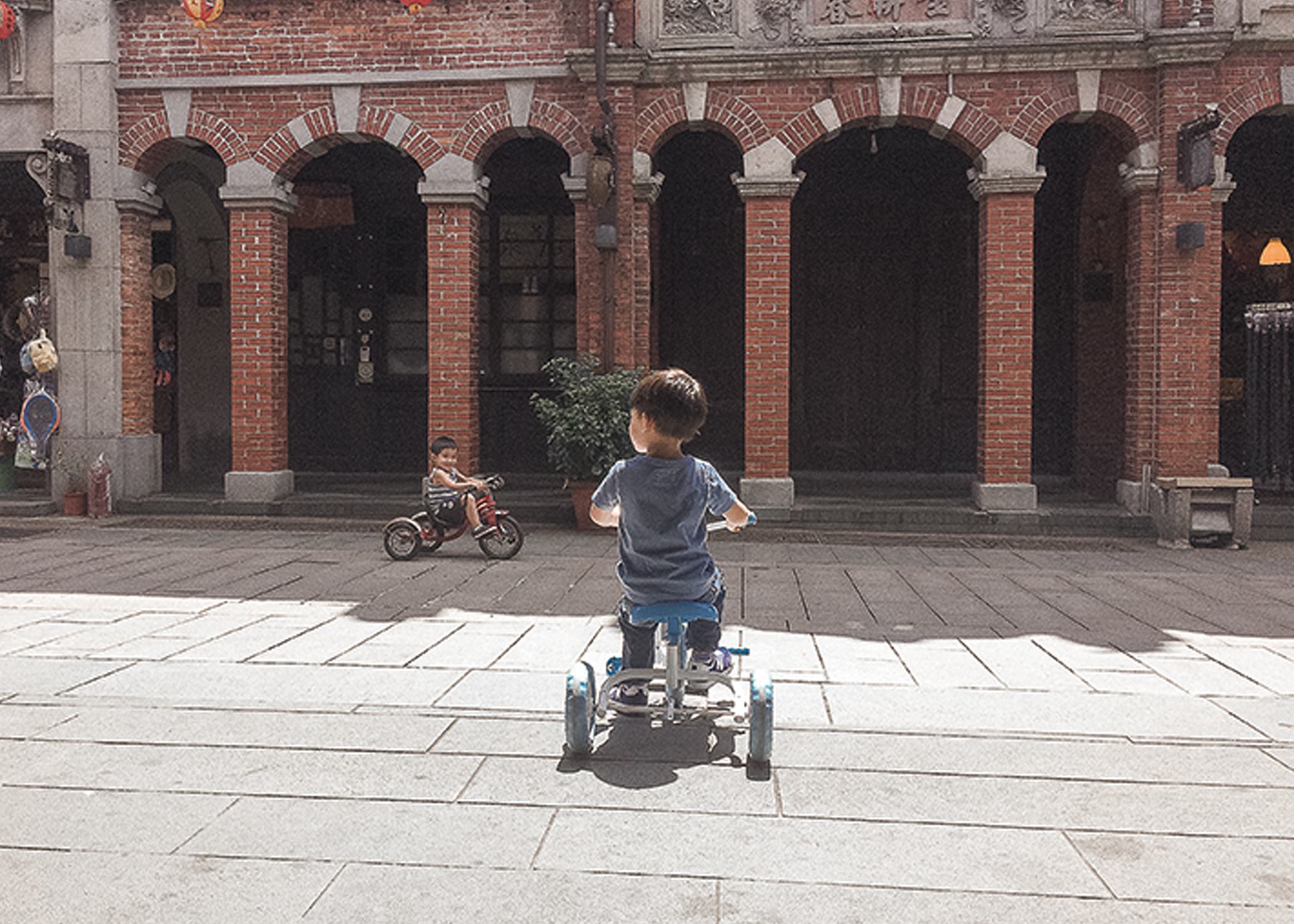 小朋友在三峽老街的紅磚立面前騎小三輪車