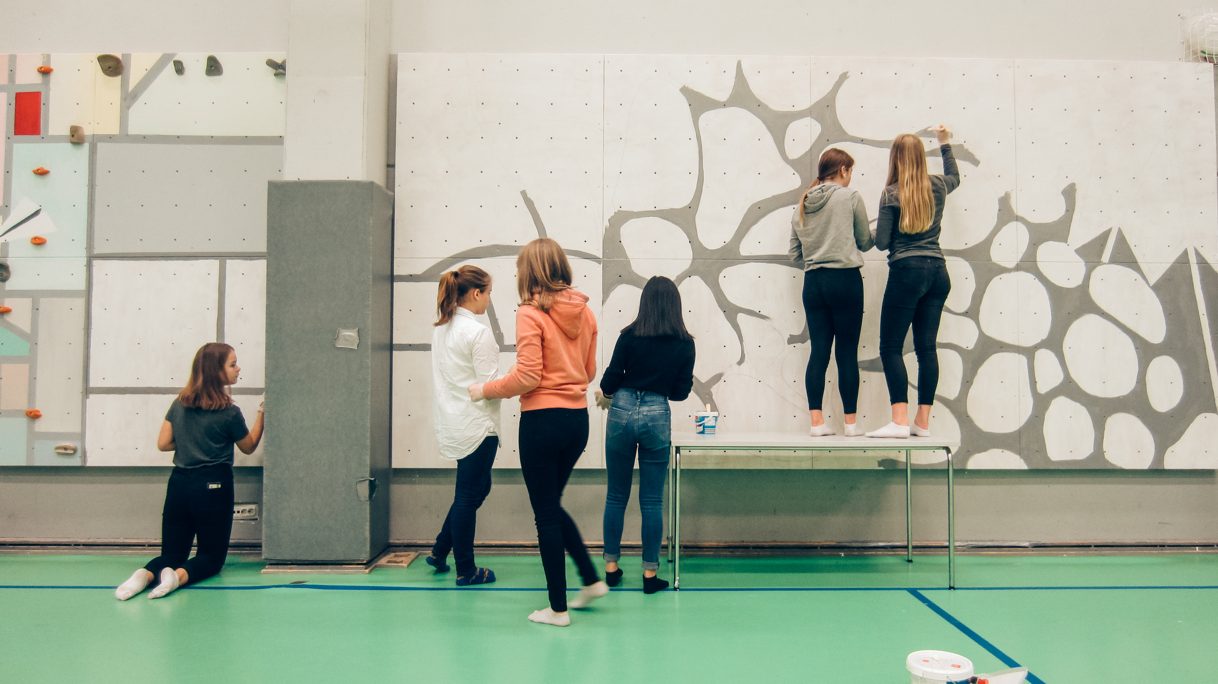 芬蘭學生在壁面上進行攀牆的彩繪創作，有兩位女學生站在桌上著色高處。