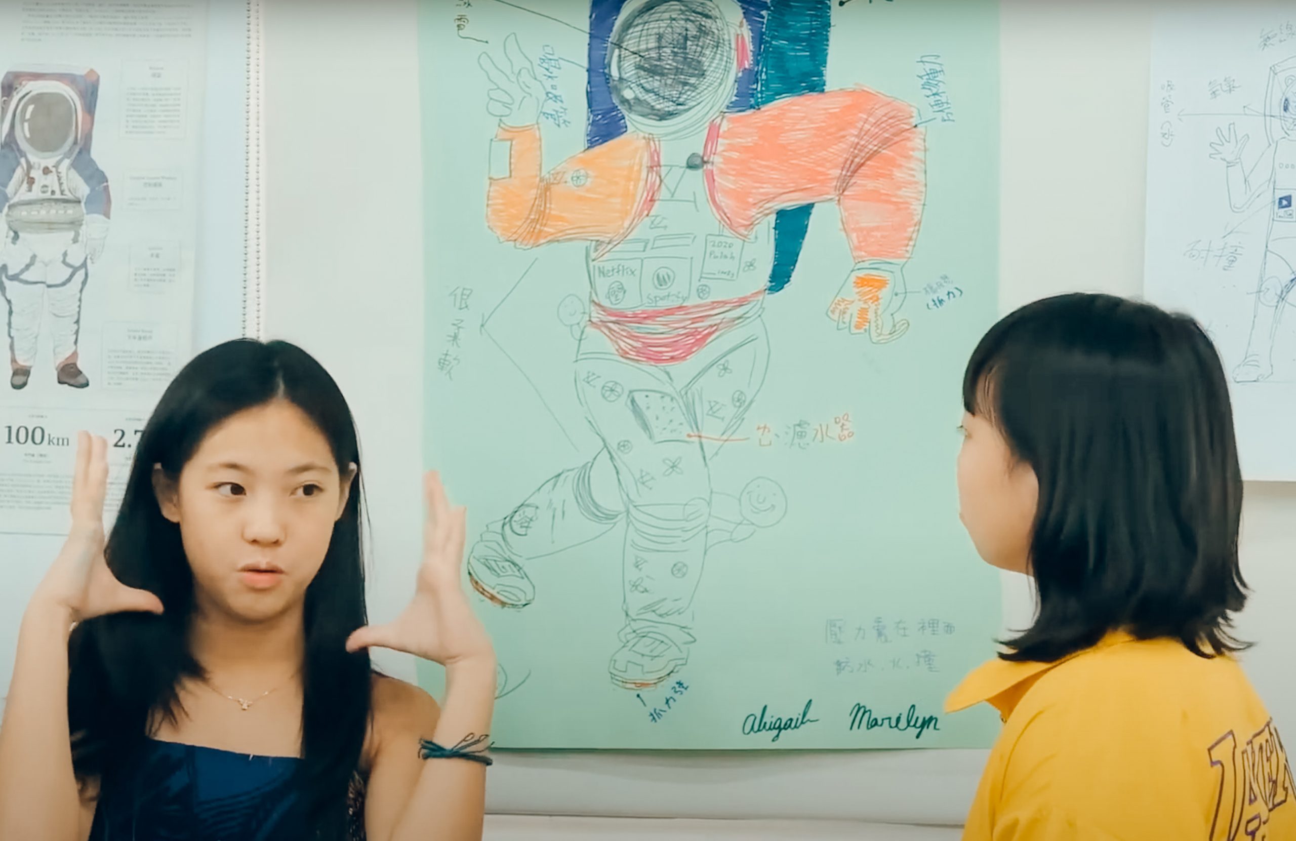 兩名學生站在自己畫的安妮新聞海報前面解說