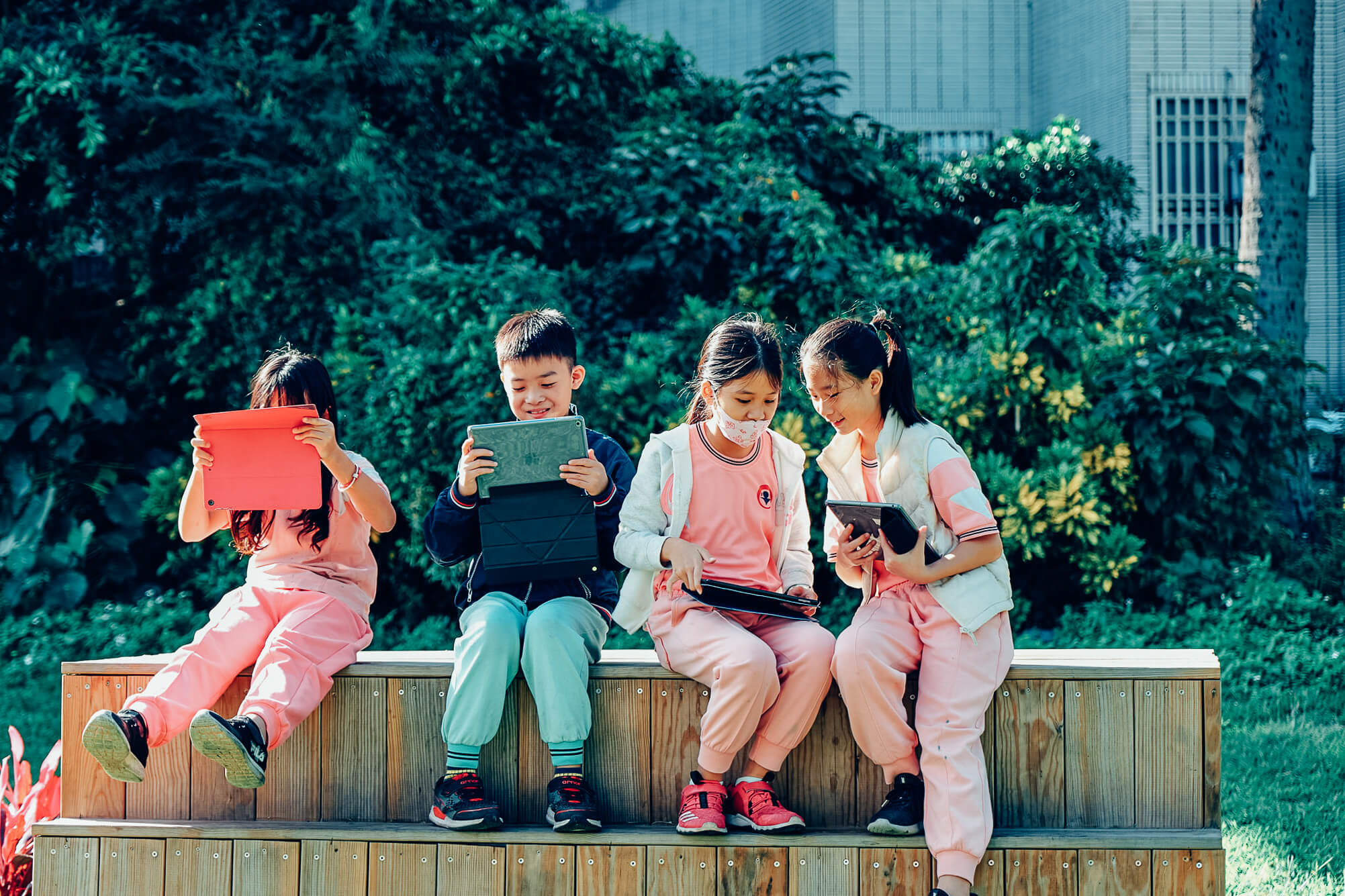 四位學童坐在校園的木製平台用平板拍攝作品畫面