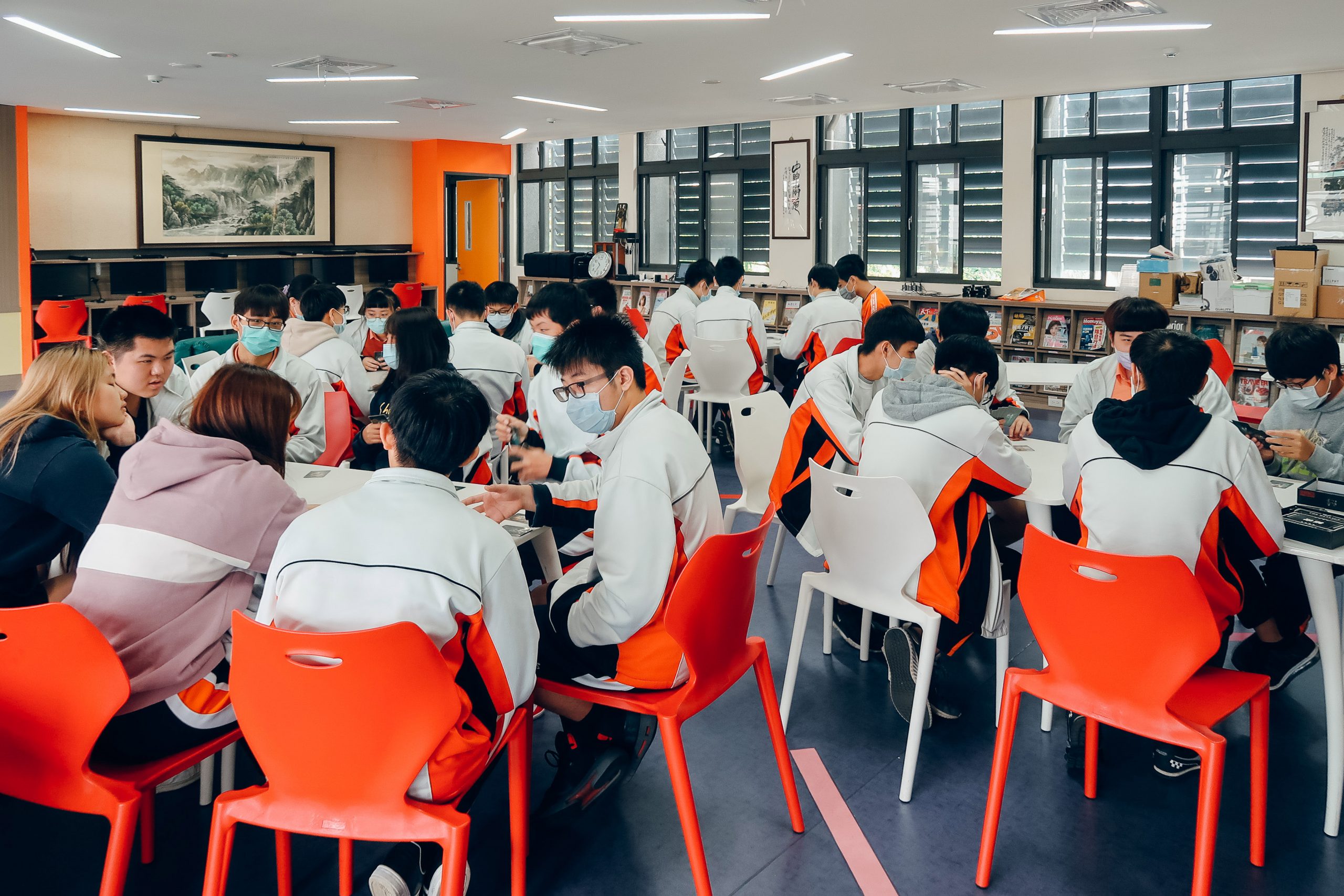 課堂中學生分組坐在紅色桌椅群討論桌遊