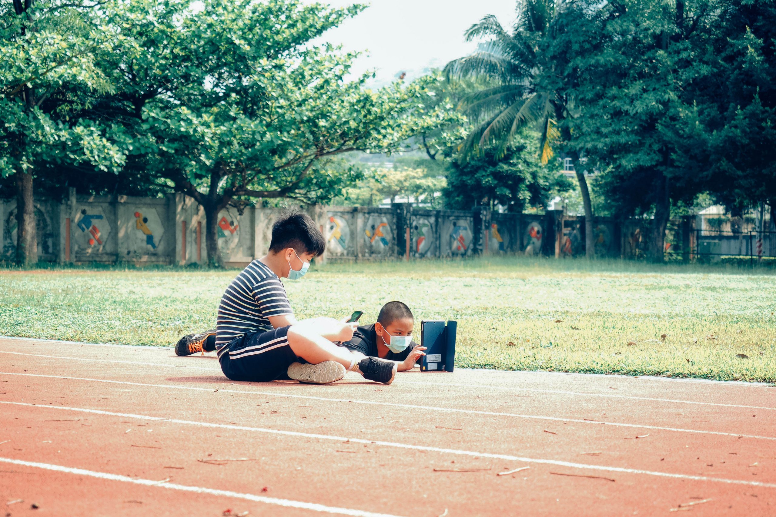 兩名男學童在自拍拼圖課程中用手機跟平板拍攝操場的畫面