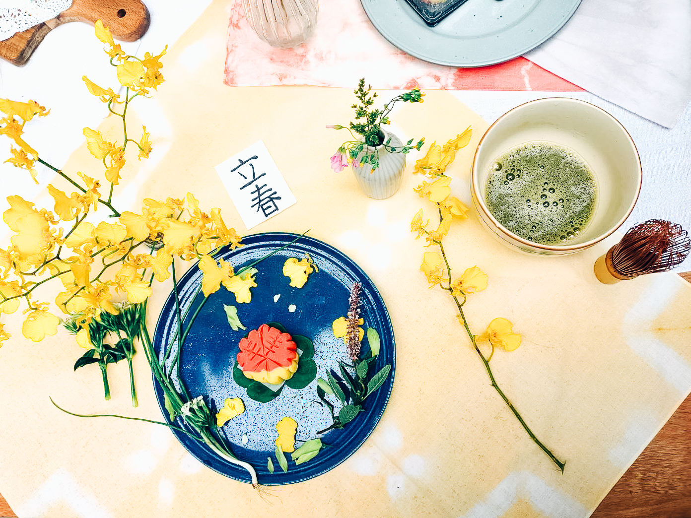 用黃色花朵與紫色花朵將月餅做擺盤，右上角又一碗剛打好的抹茶
