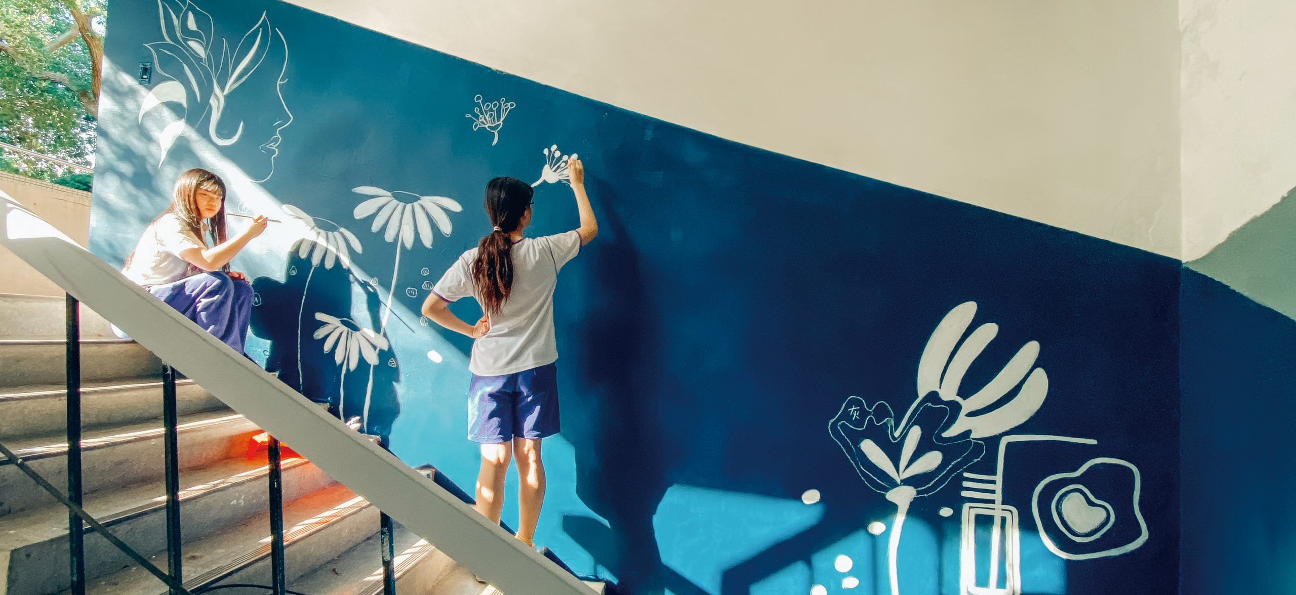 兩位學生在藍色油漆牆面上做白色塗鴉彩繪