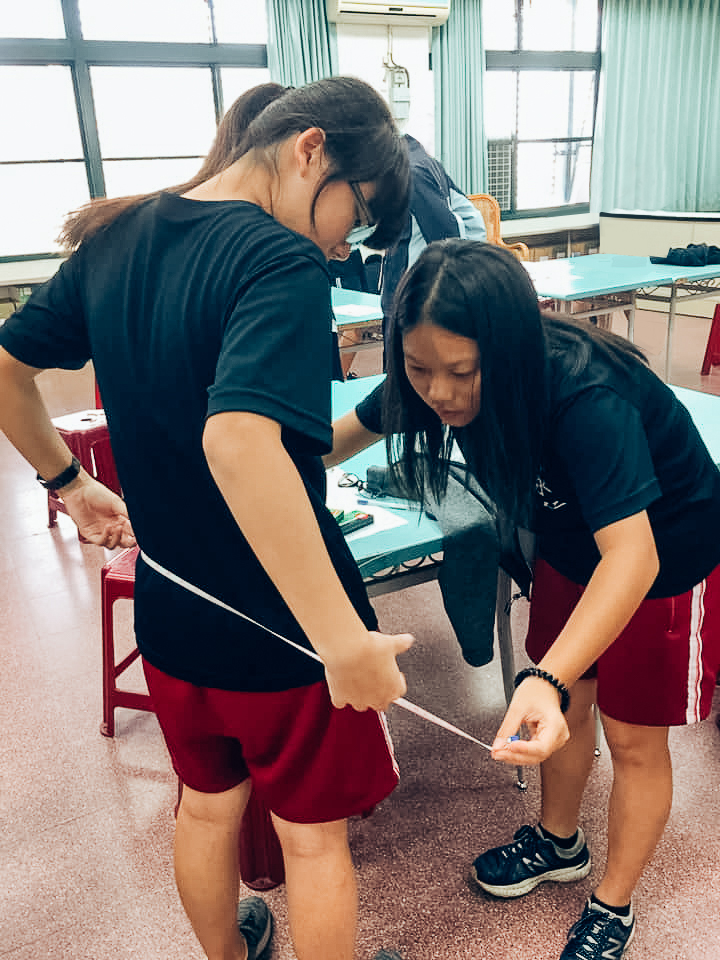 兩位女學生在為彼此的身體用皮尺做測量。